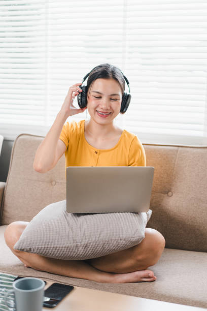 istock A young woman wearing headphones smiles while using laptop on sofa, creating relaxed and joyful atmosphere. 2171060393