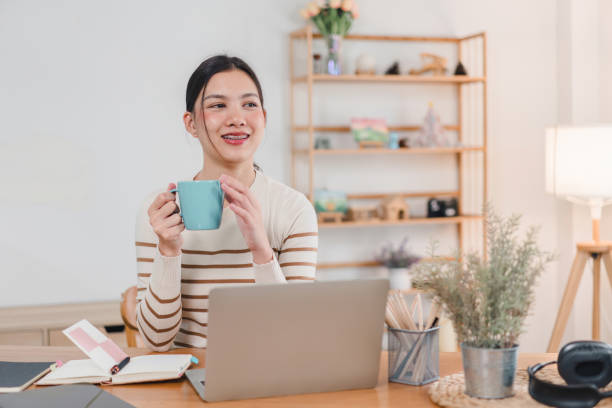 istock Smiling Asian woman typing on laptop while sitting at home, focused on work or study in a comfortable setting. 2171061193