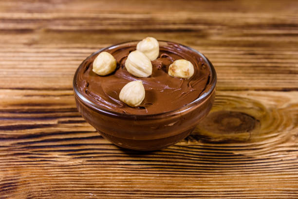Glass bowl with chocolate spread and hazelnuts on wooden table
