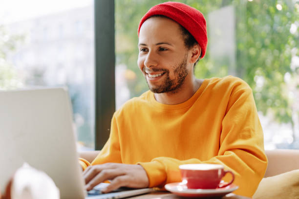 istock Smiling young man wearing stylish red hat working on laptop in cafe 2171063715
