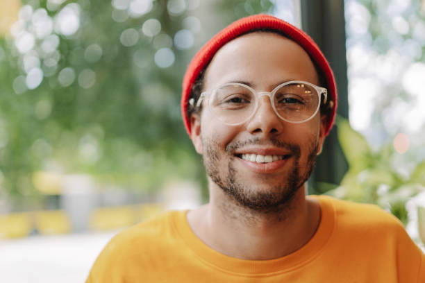 Young creative professional with a bright smile, wearing a red beanie and glasses, is enjoying the positive and inspiring atmosphere of a modern office