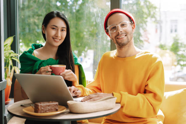 istock Young happy, smiling couple using laptop and drinking coffee in cafe looking at camera 2171063779