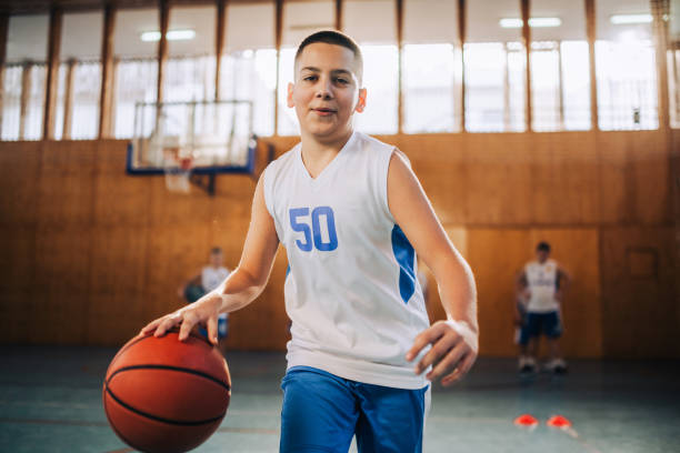 istock Kid practicing basketball in a sunny gym 2171076975
