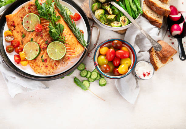 istock Grilled salmon and vegetables on wooden light background. Dinner table with cooked fish, tomatoes, asparagus 2171078151