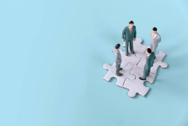 istock Four Miniature Businessmen Standing on Interlocking Jigsaw Puzzle Pieces: Symbolizing Strategic Planning and Collaboration 2171080917