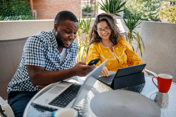 istock Young couple enjoying spending time together at home sitting on balcony and using different wireless technology while looking at mobile phone 2171093025