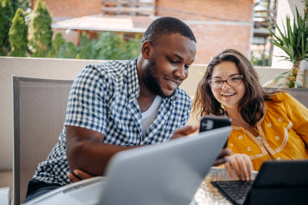 istock Young couple enjoying spending time together at home sitting on balcony and using different wireless technology while looking at mobile phone 2171093057