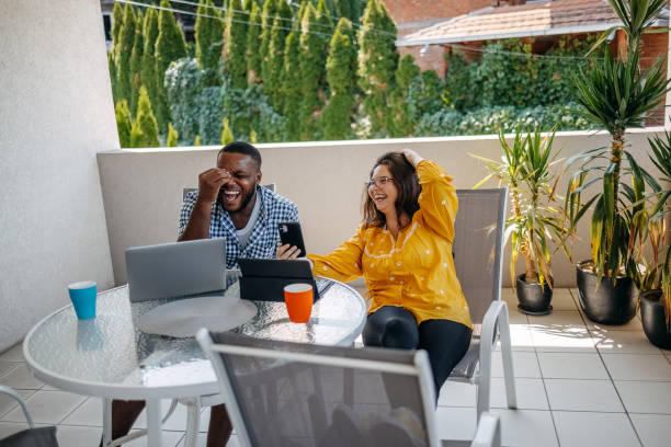 istock Young couple enjoying spending time together at home sitting on balcony and using different wireless technology while looking at mobile phone 2171093059