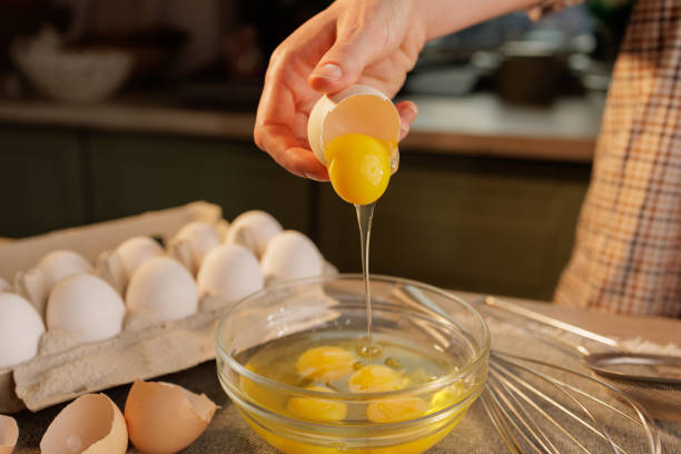 istock A person cracking an egg into a glass bowl, with several eggs in an egg carton in the background 2171093893