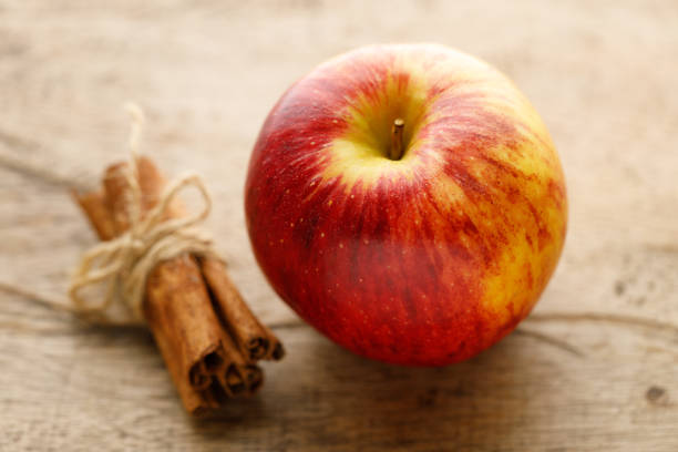 A vibrant red apple paired with aromatic cinnamon sticks, showcasing a classic combination of fresh, natural ingredients on a clean white background