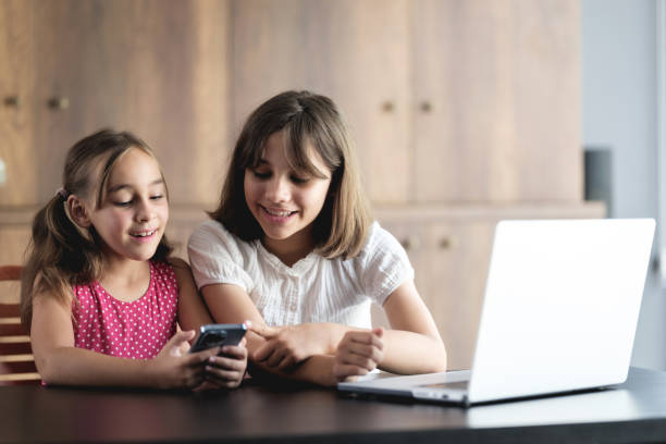 istock Little sisters having fun at home using smartphone and laptop computer 2171100771