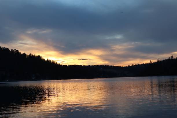 istock Serene sunset over a calm lake with forested hills. 2171101605