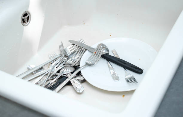 White ceramic kitchen sink full with dirty unwashed dishes, dark grey table