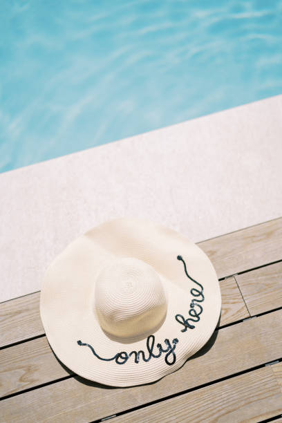 Straw hat lies on the edge of the pool. Caption: Only here. High quality photo