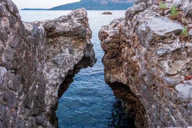 A natural rock crevice opens up to the calm blue water, creating a striking contrast between the rugged rocks and serene sea.