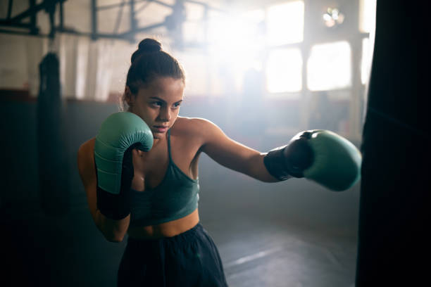istock Young Caucasian woman, with boxing gloves, punching the punching bag, while practicing kickbox in the gym 2171113802