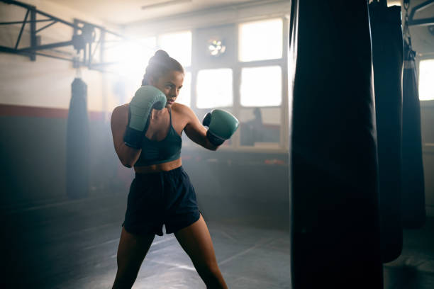 istock Young Caucasian woman, with boxing gloves, punching the punching bag, while practicing kickbox in the gym 2171113805