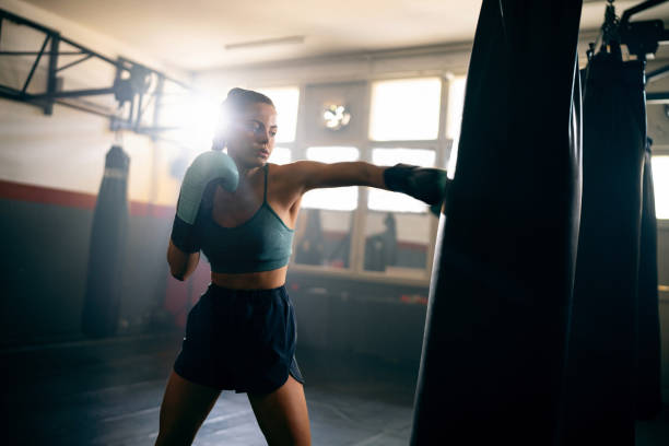 istock Young female kickboxer, with boxing gloves, punching the punching bag, while practicing kickbox in the gym 2171113911