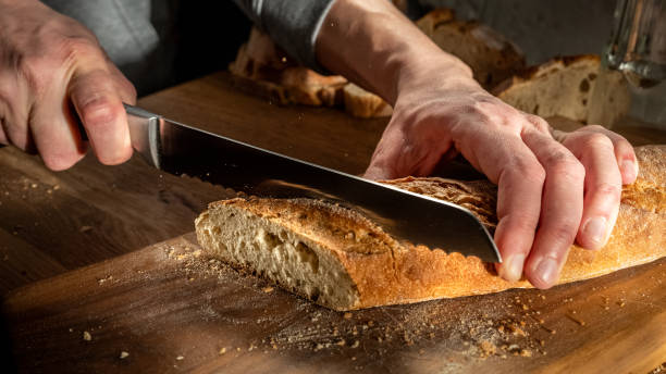 istock Slicing Fresh Bread with a Serrated Knife on a Wooden Surface 2171117086