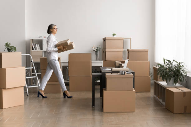 istock Woman carrying cardboard boxes in room filled with stacked parcels 2171126422