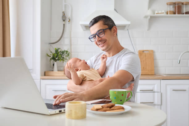 istock Smiling happy man running e-commerce business from home while looking after kid managing job responsibilities and taking care of newborn son organized workplace at home kitchen 2171134914