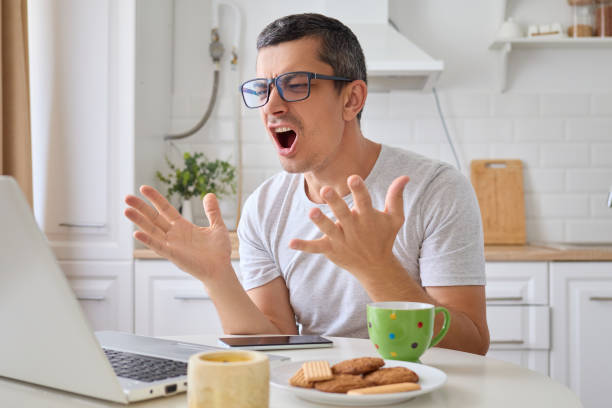 istock Despair man sitting at table in kitchen working on laptop angrily yelling at screen while browsing website frustrated by slow internet connection overwhelmed with remote job tasks 2171136017