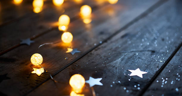 Warm glowing string lights and star decorations scattered on a rustic wooden table, creating a cozy holiday ambiance