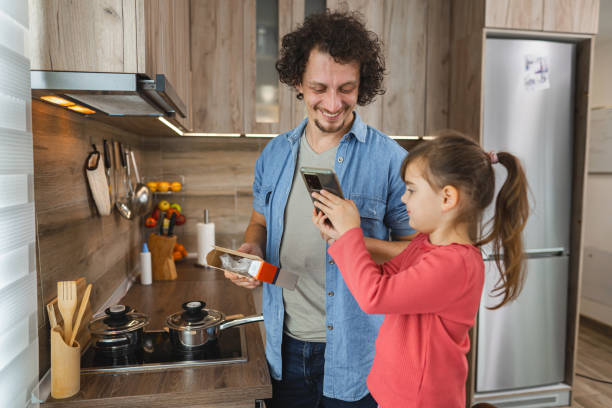 istock Dad and daughter enjoying quality time together in a cozy kitchen while preparing a meal and capturing moments with a smartphone 2171140087
