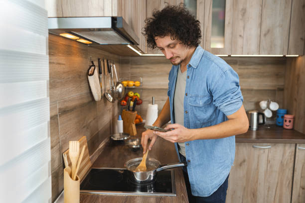 istock A creative cook stirring a flavorful dish while checking a recipe on a smartphone in a cozy wooden kitchen setting 2171141877