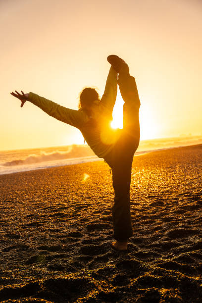 A woman is doing a yoga pose on a beach at sunset. Concept of relaxation and tranquility, as the woman stretches her body in the warm, golden light of the setting sun