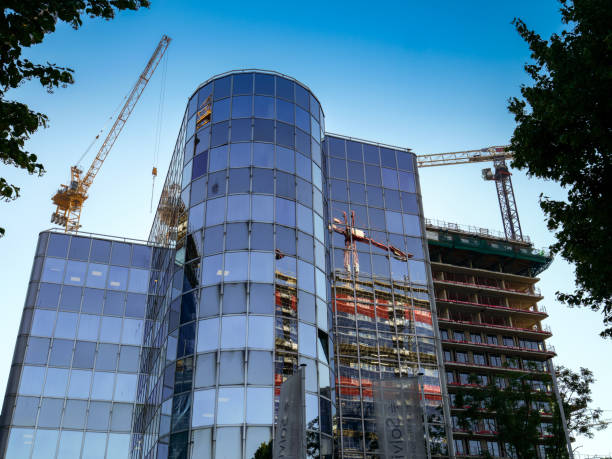 Looking up at the construction site of a high-rise building with two cranes in the foreground. Other construction side seen in the reflections.