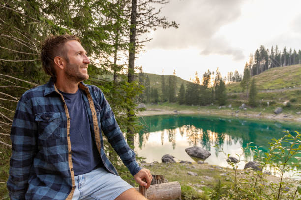 istock Man sitting by a serene alpine lake in a peaceful forest 2171153681