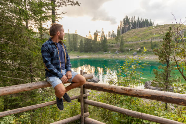 istock Man sitting by a serene alpine lake in a peaceful forest 2171153829