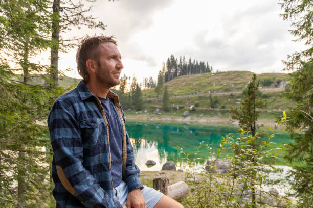 istock Man sitting by a serene alpine lake in a peaceful forest 2171154202