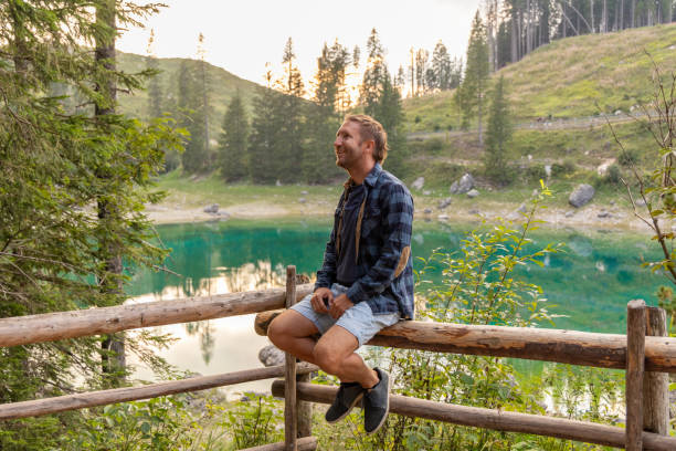 istock Man sitting by a serene alpine lake in a peaceful forest 2171154367