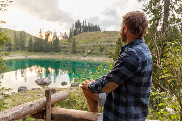 istock Man sitting by a peaceful alpine lake enjoying the view 2171154718