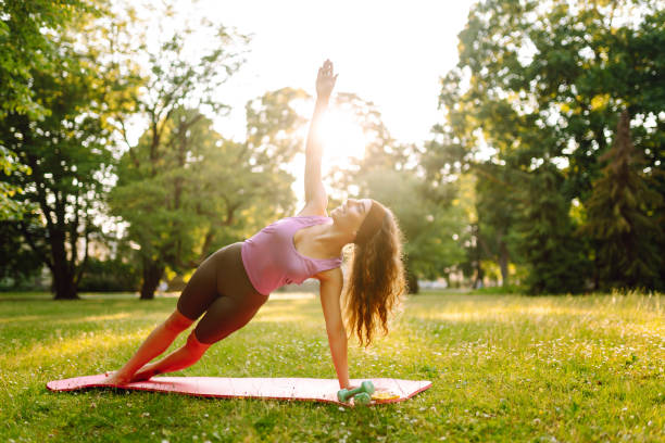 istock A woman practices yoga in a sunlit park while using a mat and weights on a warm afternoon. 2171162065