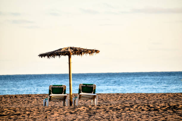 istock Two beach chairs are on the sand next to a small umbrella 2171163738