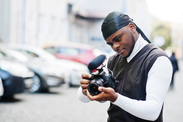 istock Young professional african american videographer holding professional camera with pro equipment. Afro cameraman wearing black duraq making a videos. 2171164501