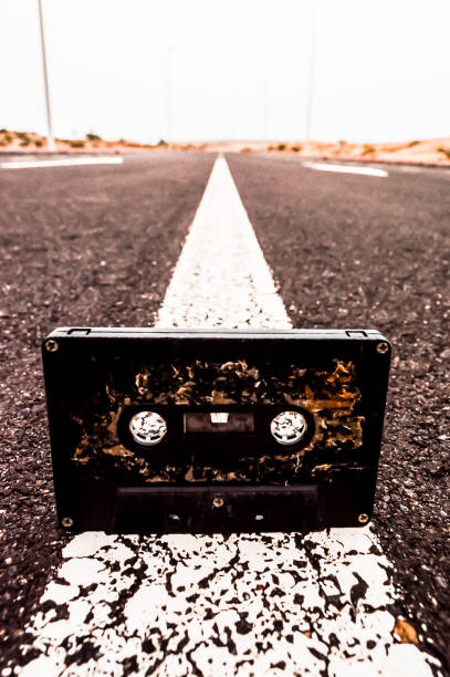A black cassette tape is laying on the road. The tape is old and worn, and it is laying on the road in the middle of the street. The scene is quiet and peaceful