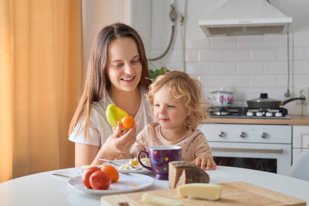 istock Happy mother feeding hungry toddler daughter with nutritious dish in kitchen while enjoying fun moment of motherhood at home offering fresh paper to eat 2171166795