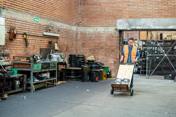 A factory worker pushes a cart loaded with pipes, moving carefully around the shop floor while making sure that each piece arrives at its destination accurately and safely.