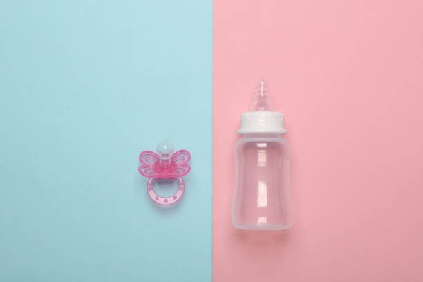 Bottle for feeding newborn and pacifier on a blue-pink background
