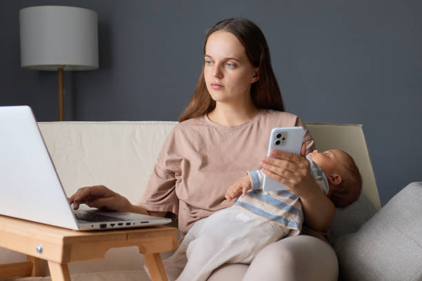 istock Serious concentrated mother teleworking from her apartment using her PC and cellphone to stay connected while caring for her newborn during maternity leave doing her remote job tasks 2171171225