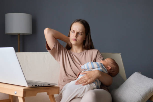 istock Exhausted woman sitting on couch with her baby using her laptop to work online while her infant sleeping balancing remote work with family time massaging painful neck 2171171232