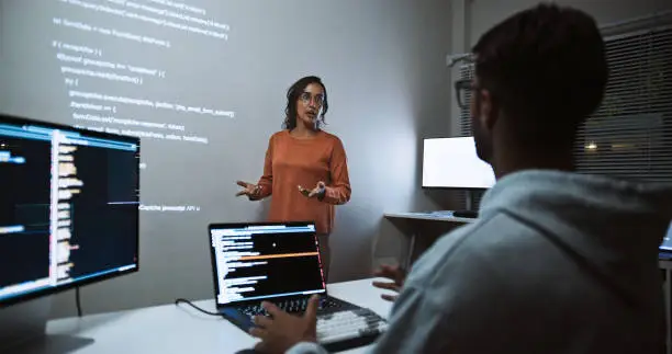 Photo of Hispanic Latin American software engineer developer use laptop computer program coding, projection screen presentation. Programming language development, business technology, night work people concept