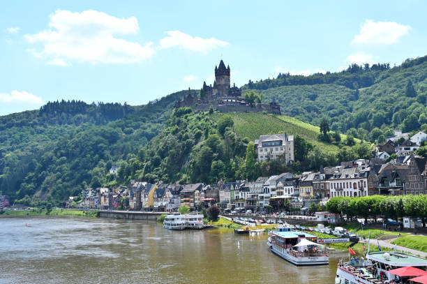 Reichsburg Cochem Castle stands proudly above the town of Cochem, surrounded by lush greenery and the rolling hills of the Moselle Valley, showcasing its medieval