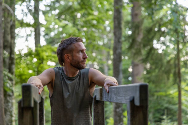 A man takes a thoughtful break, resting on a wooden railing surrounded by a lush forest.
