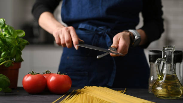 istock Woman In Chief Apron Sharpening A Knife In Kitchen 2171204797