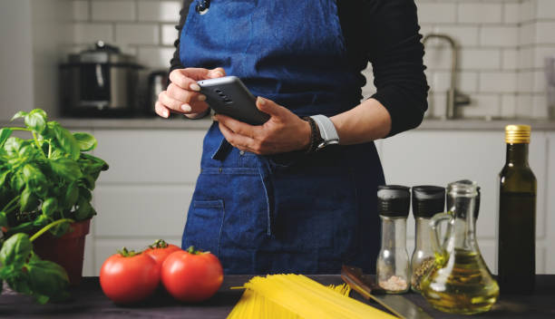 istock Girl In Apron Typing A Message On A Smartphone In The Kitchen 2171204820